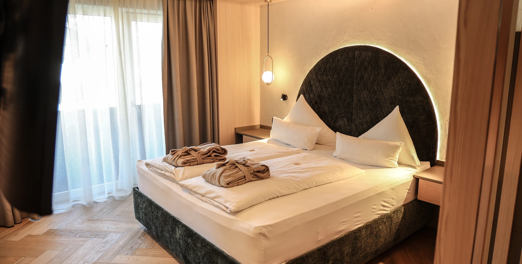 Modern eingerichtetes Zimmer mit Doppelbett und rundem Wandspiegel im Metzgerwirt Zillertal.