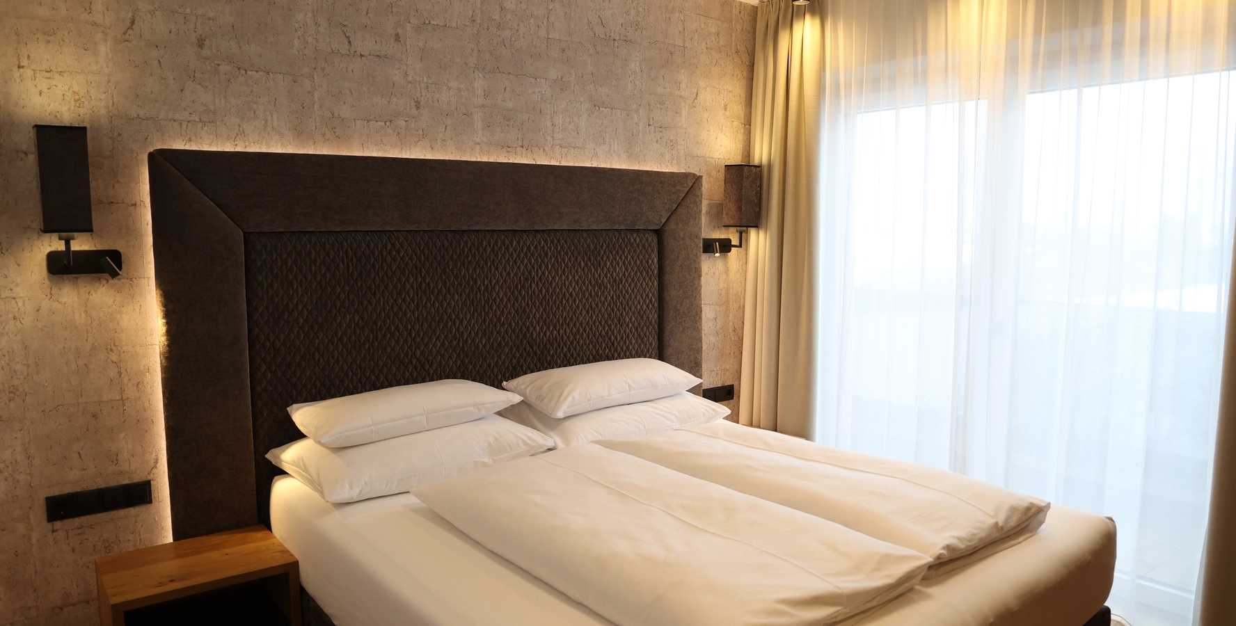 Zimmer mit bezogenem Doppelbett und großem Fenster zum Balkon in der Junior Suite a