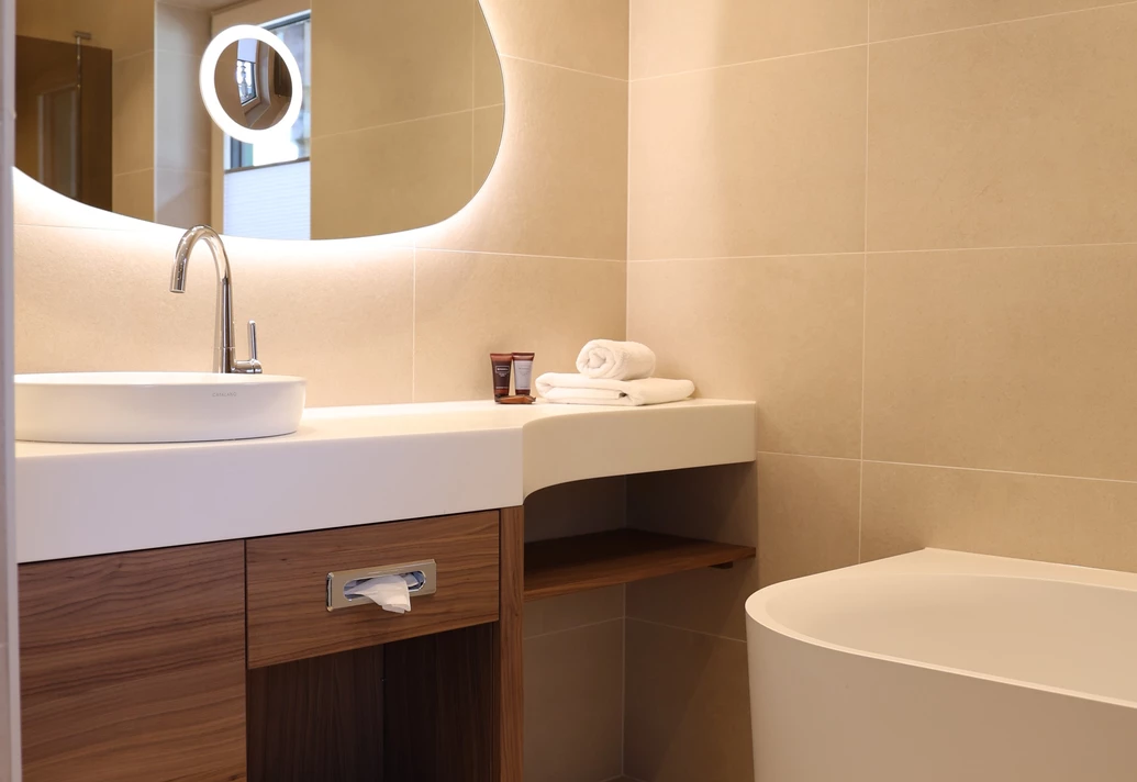 Helles Badezimmer mit Waschtisch, beleuchtetem Spiegel und Badewanne im Doppelzimmer Lifestyle Komfort.