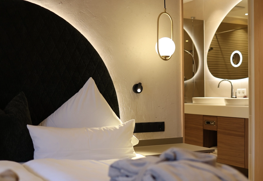 Gemütliches Bett mit moderner Pendelleuchte und Blick auf den Waschtisch im Doppelzimmer Lifestyle Classic.